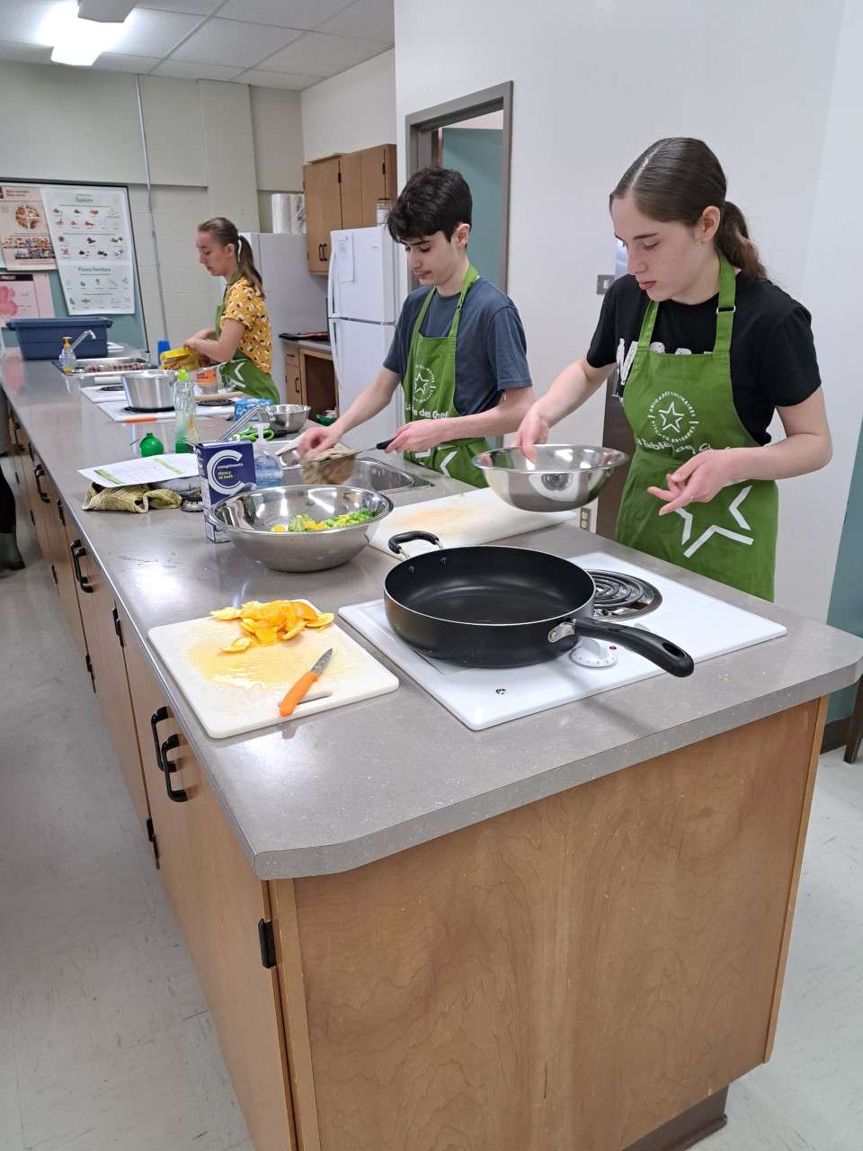 Les jeunes cuisiniers en pleine action. On y voit trois élèves en train de cuisine à leur poste de travail respectif. 